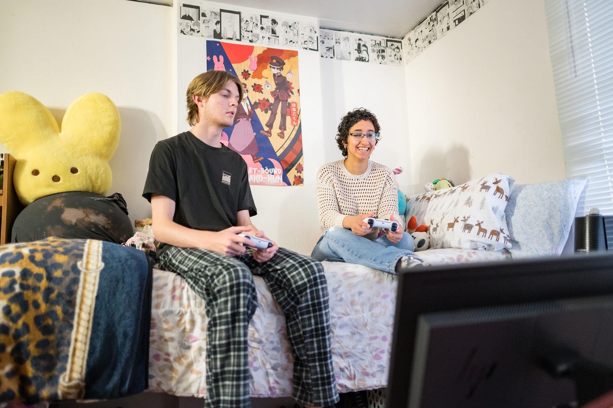 Mal and Femal Student sitting on their bed in a dorm room watching tv