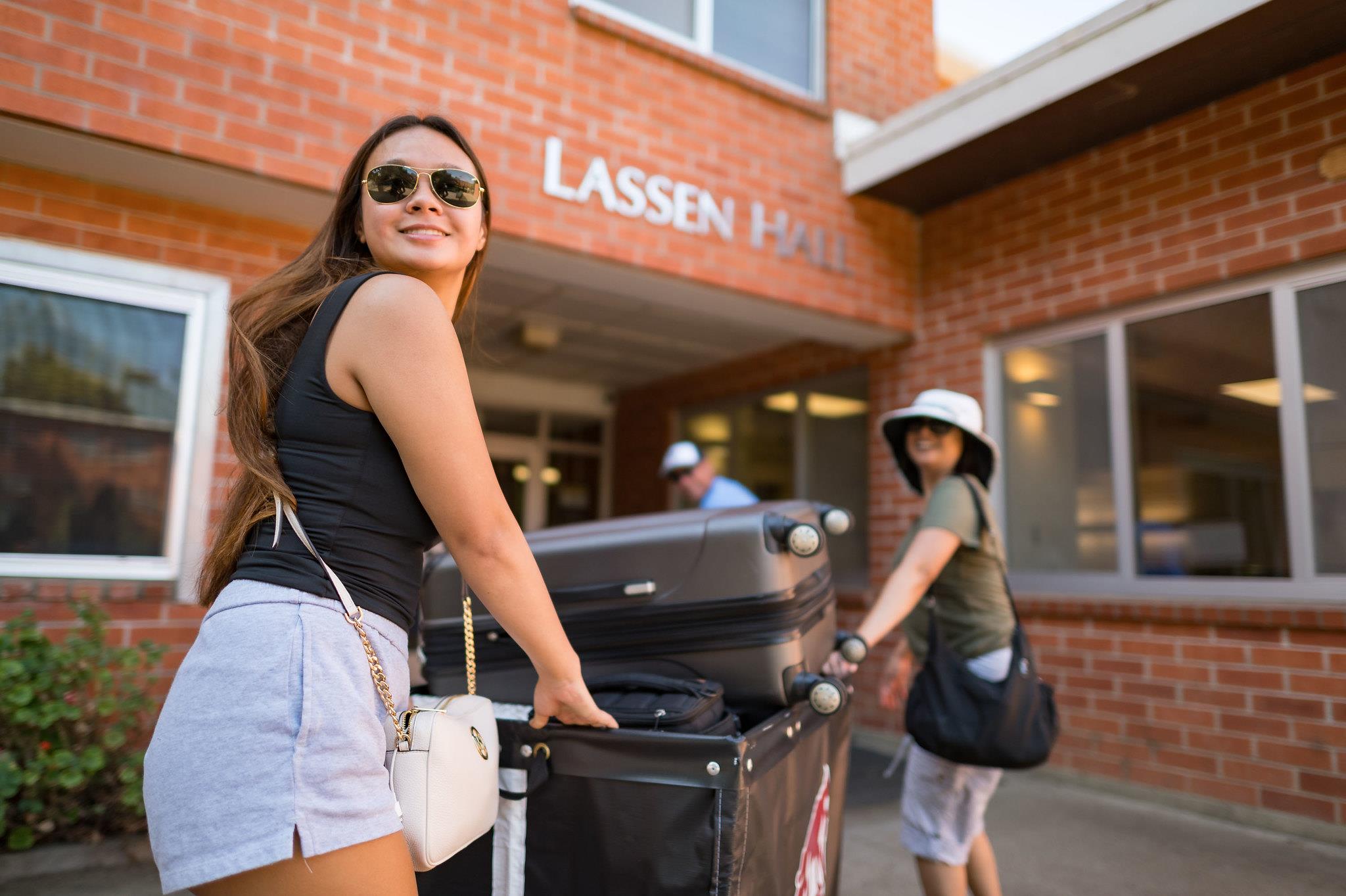 Female student in sunglasses pushing a cart full of belongings into Shasta Hall