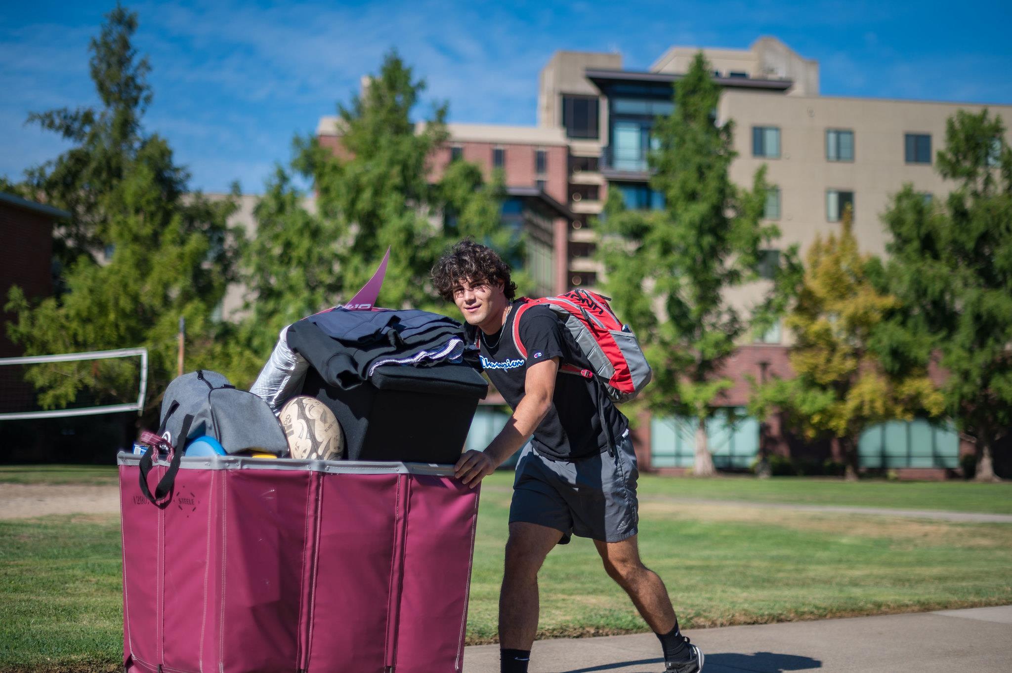 Male Student in Sunglasses Pushing a cart full of belongings down a walkway between Lassen and Shasta Halls